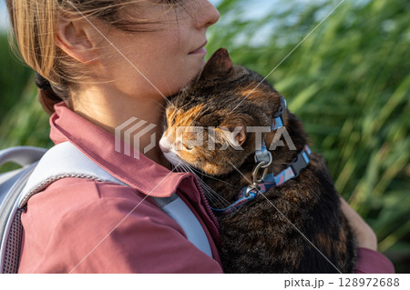 Scared cautious cat embrace woman on shoulder, hiding in new nature surroundings on walk together 128972688