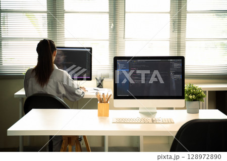 Modern workspace shows coding monitors with female developer working in background 128972890