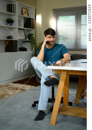 Freelancer sitting at a desk and chatting on the phone in a modern home 128972929