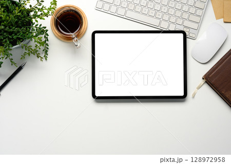 Top view of office desk with blank tablet screen, coffee cup, and green plant Top view of office desk with blank tablet screen, coffee cup, and green plant 128972958
