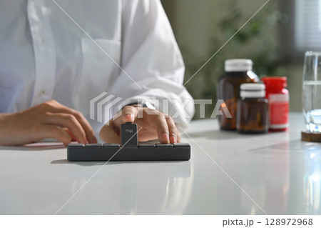 Close up of person organizing daily medication on desk. Health and medication concept 128972968