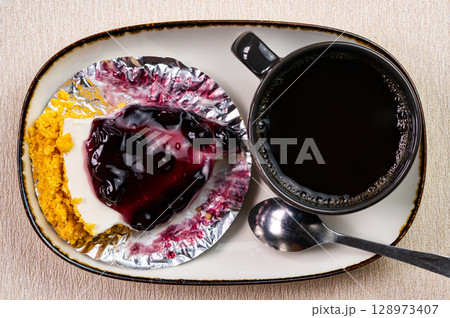 Top view of blueberry cheese pie on foil paper and a cup of coffee in black ceramic cup. Top view of blueberry cheese pie on foil paper and a cup of coffee in black ceramic cup. 128973407
