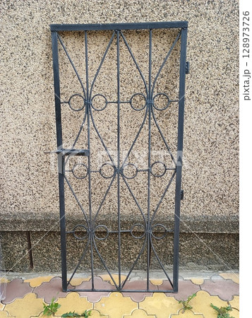 Wrought Iron Window Security Grille on Textured Concrete Wall, Dark Blue Metal Bars, Circular Motifs, Outdoor Home Protection, Decorative Design Element 128973726