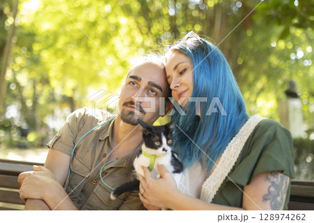 Young couple holding a kitten are enjoying a sunny day in the park Young couple holding a kitten are enjoying a sunny day in the park 128974262
