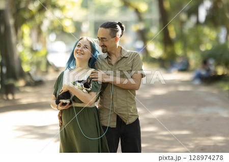 Happy couple walking a cat on a leash in a park Happy couple walking a cat on a leash in a park 128974278