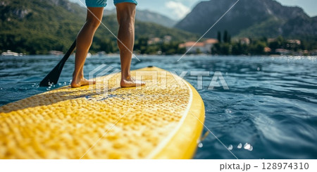 Legs of man standing on paddleboard on Calm Mountain Lake. SUP Stand-up Paddleboard 128974310