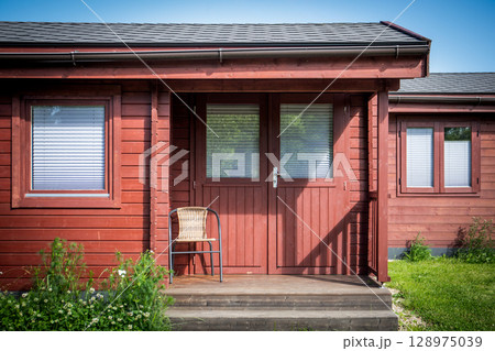 Front View of Red Wooden Cabin with Chair and Windows in Summer Countryside Setting Front View of Red Wooden Cabin with Chair and Windows in Summer Countryside Setting 128975039