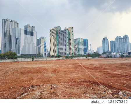 A row of skyscrapers surrounds the red dirt field. 128975253