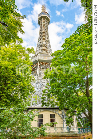 Petrin Lookout Tower rises above the lush trees, offering stunning views of Prague. Visitors enjoy the vibrant surroundings while climbing to the observation deck for breathtaking scenery. 128975544