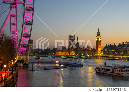 Stunning view capturing the London Eye, Westminster Palace, and Big Ben illuminated at dusk. The tranquil River Thames reflects the vibrant colors of the evening sky. Stunning view capturing the London Eye, Westminster Palace, and Big Ben illuminated at dusk. The tranquil River Thames reflects the vibrant colors of the evening sky. 128975548