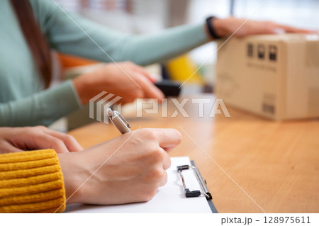 Closeup hand woman writing document while scanning package with barcode reader. Closeup hand woman writing document while scanning package with barcode reader. 128975611