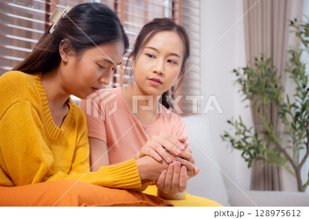 Young asian woman comforting friend with crying and depression sitting on sofa in living room. Young asian woman comforting friend with crying and depression sitting on sofa in living room. 128975612