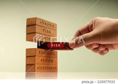Hand pulls a block labeled RISK from stack of wooden blocks representing structured plans. Core of financial and business risk management 128977033