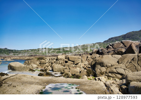 A scenic coastal landscape in Ireland, with a clear blue sky, rocky formations, and serene atmosphere. A scenic coastal landscape in Ireland, with a clear blue sky, rocky formations, and serene atmosphere. 128977593