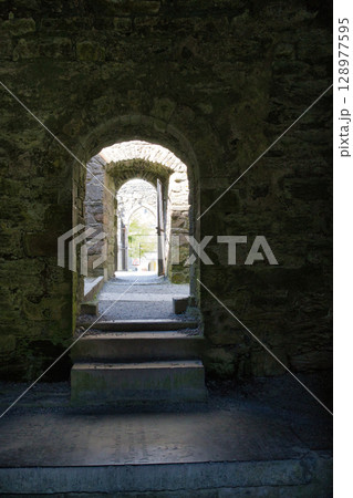 A series of stone archways in an old Irish castle, leading to an open doorway, with steps. A series of stone archways in an old Irish castle, leading to an open doorway, with steps. 128977595