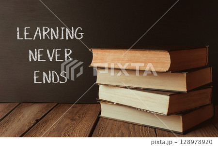 A stack of books with the words learning never ends written on a chalkboard 128978920