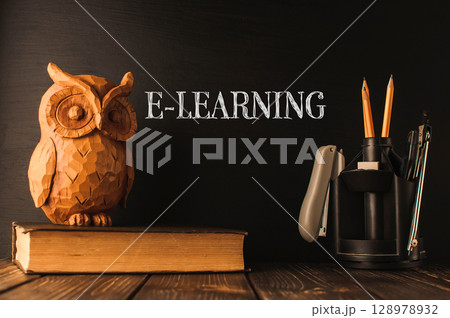 A wooden owl sits on top of a stack of books 128978932