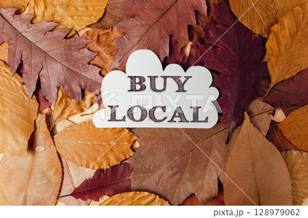 A white sign that says Buy Local is on top of a pile of leaves 128979062