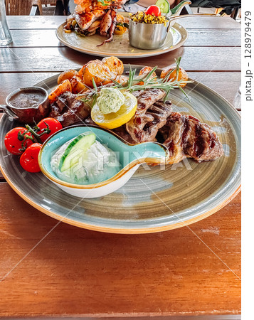 Plate of food with a variety of meats and vegetables, including tomatoes 128979479