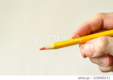 Yellow pencil with a red tip is being held by a person 128980211
