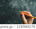 Person is holding a pencil and writing on a chalkboard 128980276