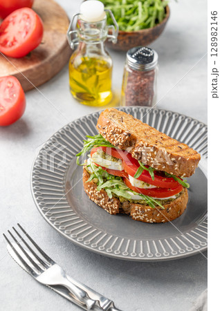 Healthy sesame toast with tomatoes, mozzarella, arugula and pesto on a plate on light background Healthy sesame toast with tomatoes, mozzarella, arugula and pesto on a plate on light background 128982146