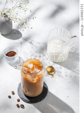 Ice latte coffee in a glass with milk on a light background with bouquet of flowers Ice latte coffee in a glass with milk on a light background with bouquet of flowers 128982151