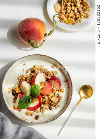 Natural greek yogurt with granola or muesli, peach and mint in a bowl on a white background 128982162