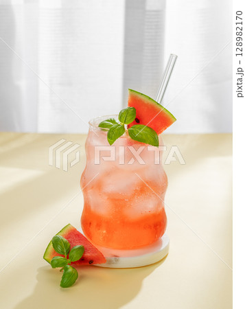 Watermelon mojito cocktail with ice and mint in a glass on a marble stand on a yellow table 128982170