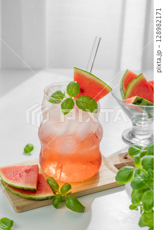 Watermelon mojito cocktail with ice and mint in a glass on a wooden board on a white table 128982171
