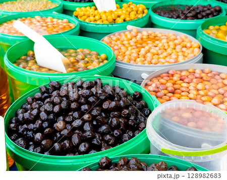 Variety of fresh olives in green buckets at a market stall 128982683