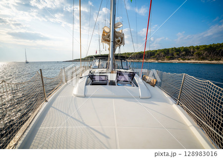 Sailing yacht anchored near uninhabited islands in Croatia, captured from the bow. Peaceful summer stopover and maritime leisure in a remote coastal area. Sailing yacht anchored near uninhabited islands in Croatia, captured from the bow. Peaceful summer stopover and maritime leisure in a remote coastal area. 128983016