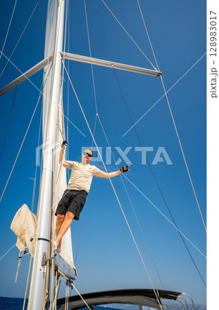 Man climbing the mast of a sailing yacht with full sails, captured from above near Croatia. Courage, freedom, yachting lifestyle and maritime exploration. Man climbing the mast of a sailing yacht with full sails, captured from above near Croatia. Courage, freedom, yachting lifestyle and maritime exploration. 128983017