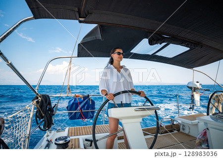 Young woman steering a sailing yacht near Croatia, confidently standing at the helm. Female leadership, empowerment and freedom in maritime lifestyle. 128983036