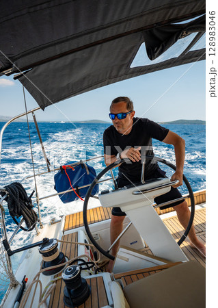 Man standing at the helm of a sailing yacht near Croatia, steering the boat through open water. Leadership, control, sailing lifestyle and freedom at sea. 128983046