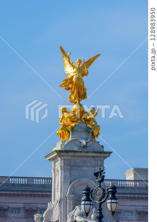 A striking golden statue of Queen Victoria atop the memorial stands proud outside Buckingham Palace on a clear day. The intricate details capture the monument's historical significance in England. A striking golden statue of Queen Victoria atop the memorial stands proud outside Buckingham Palace on a clear day. The intricate details capture the monument's historical significance in England. 128983950