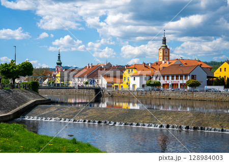 A picturesque view of the Otava River flows gently through Susice, showcasing charming architecture and colorful houses mirrored on the water's surface under a blue sky. A picturesque view of the Otava River flows gently through Susice, showcasing charming architecture and colorful houses mirrored on the water's surface under a blue sky. 128984003
