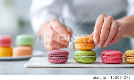 Person carefully stacking colorful macarons during dessert making process creating delightful and vibrant sweet treat arrangement 128984272