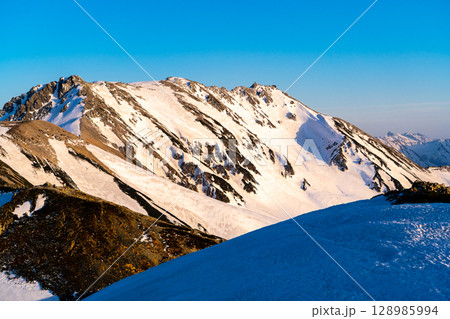 夕日に染まる立山連峰の雄山、大汝山（剱御前からの景色）　残雪期の北アルプス立山・別山登山 128985994