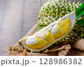 Ripe durian fruit or Durio zibethinus with yellow creamy pulp exposed on wood background. 128986382