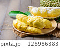 Ripe durian fruit or Durio zibethinus with yellow creamy pulp exposed on wood plate 128986383