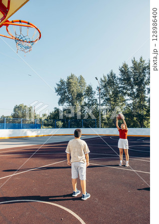 playground basketball practice with boy and girl in casual clothes, large open court with copy space, concept of teen wellness, afterschool sport program 128986400
