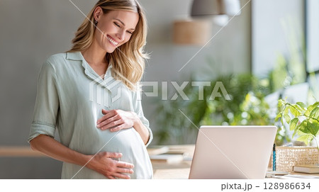 Happy pregnant mom working remotely on laptop. Online video call. The radiant mom smiles warmly during her online meeting, embodying the essence of working mothers. 128986634