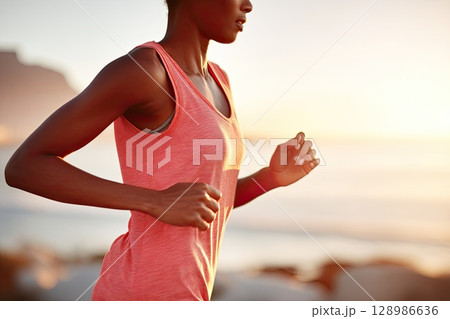 Portrait of a young woman running on the beach during sunset. The golden sunset reflects in the waves as the young woman runs along the beach, celebrating life. 128986636