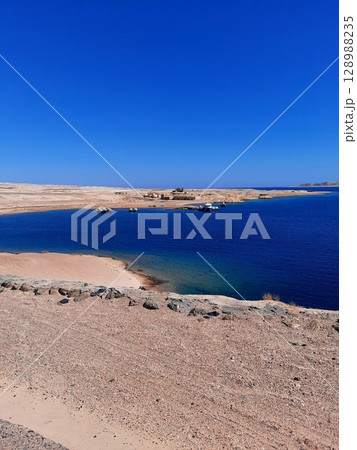 Serene Coastal Lagoon with Clear Blue Waters and Boats Under a Vibrant Blue Sky 128988235