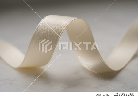 A smooth, creamy ivory ribbon gracefully undulates across a softly lit, subtly textured surface, showcasing its delicate sheen and elegant curves 128988269