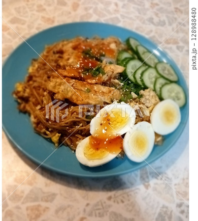 Flavorful Noodle Dish with Sliced Eggs, Cucumber, and Grilled Meat on a Blue Plate Flavorful Noodle Dish with Sliced Eggs, Cucumber, and Grilled Meat on a Blue Plate 128988480