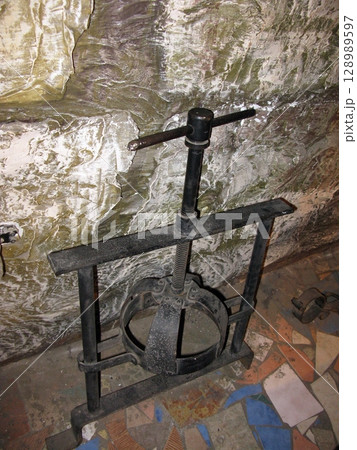 A black iron head press with a screw mechanism, set against a rugged stone wall in a dimly lit historical torture chamber 128989597