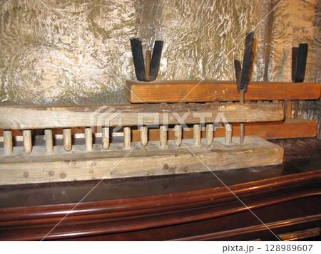 A rustic wooden tray with embedded spikes and metal supports, displayed on a stone shelf, suggesting a grim historical punishment tool 128989607