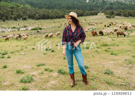 A woman wearing a plaid shirt and jeans stands in a field with a hat on A woman wearing a plaid shirt and jeans stands in a field with a hat on 128989652